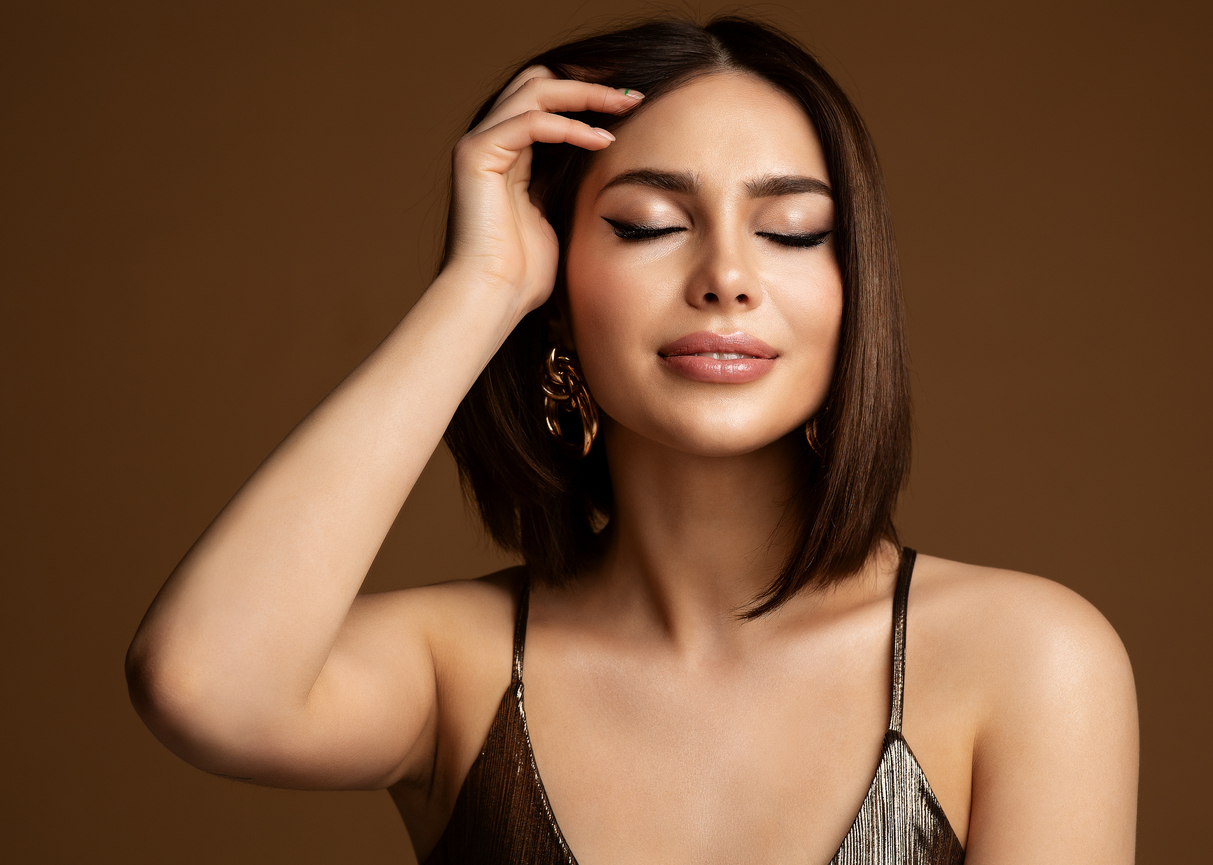 Woman with a brown bob posing with her hand moving her hair