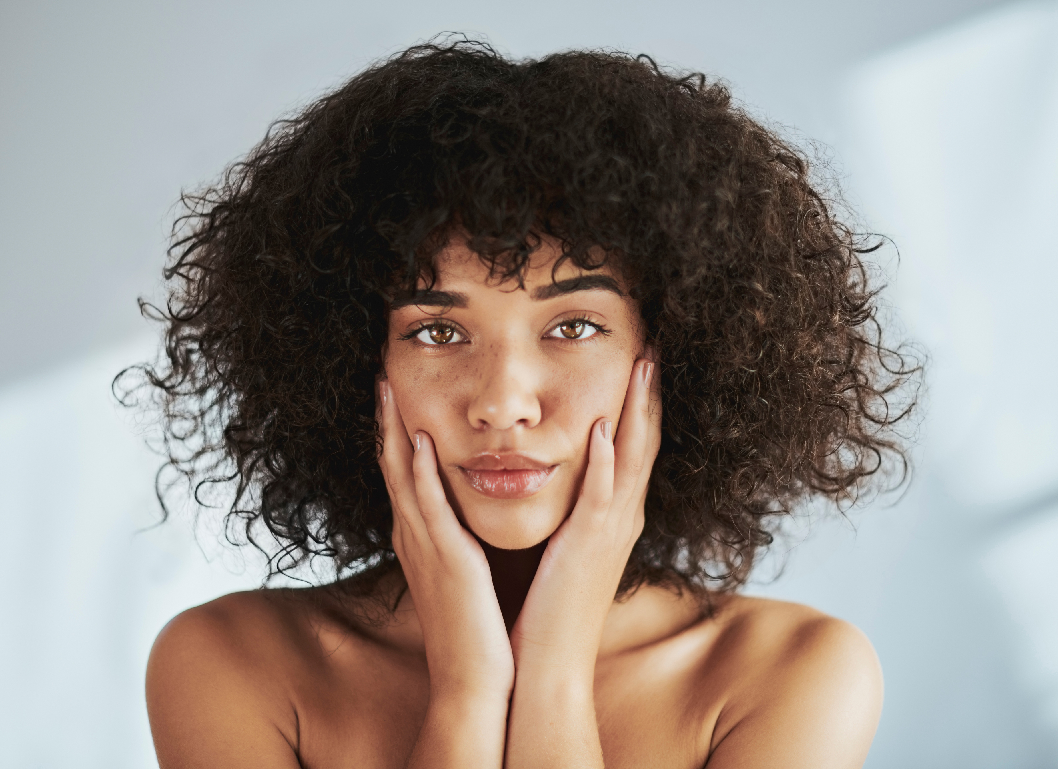 woman with curly hair holding her hands on her face